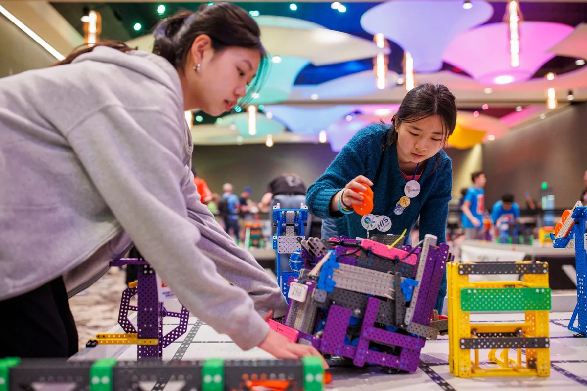 Two students adjusting a VEX IQ robot at the field edge during VEX Worlds
